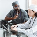Two doctors discuss patient diagnosis using laptop in hospital office.
