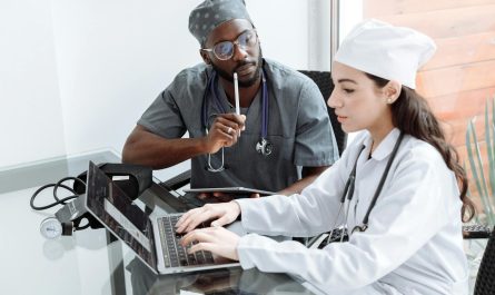 Two doctors discuss patient diagnosis using laptop in hospital office.