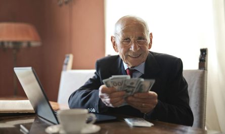 Elderly man smiling while counting cash at a home office setting.