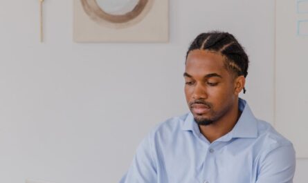 A professional man with braided hair working on a laptop in a modern office setting.